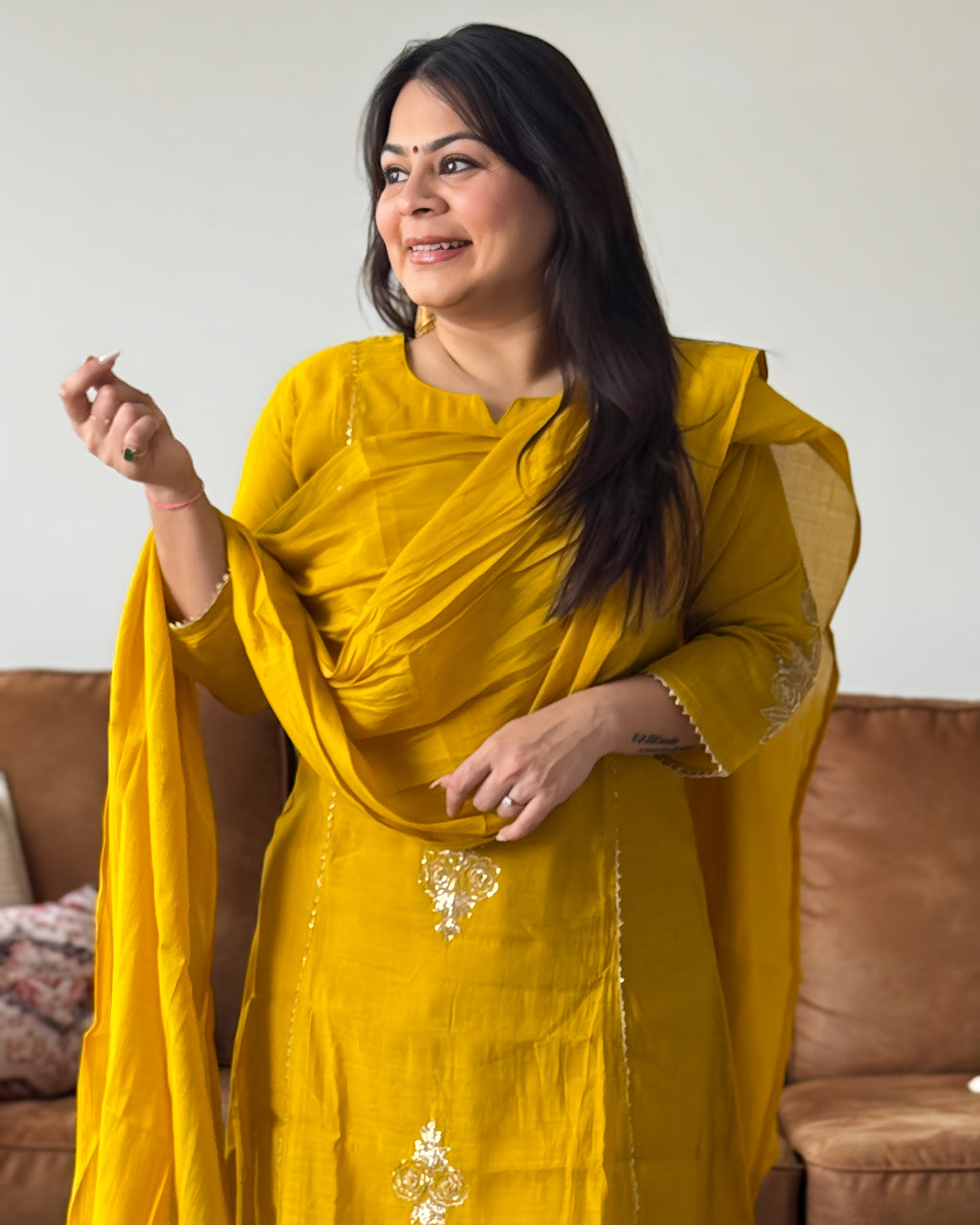 Woman wearing a yellow traditional outfit with a brown sofa in the background
