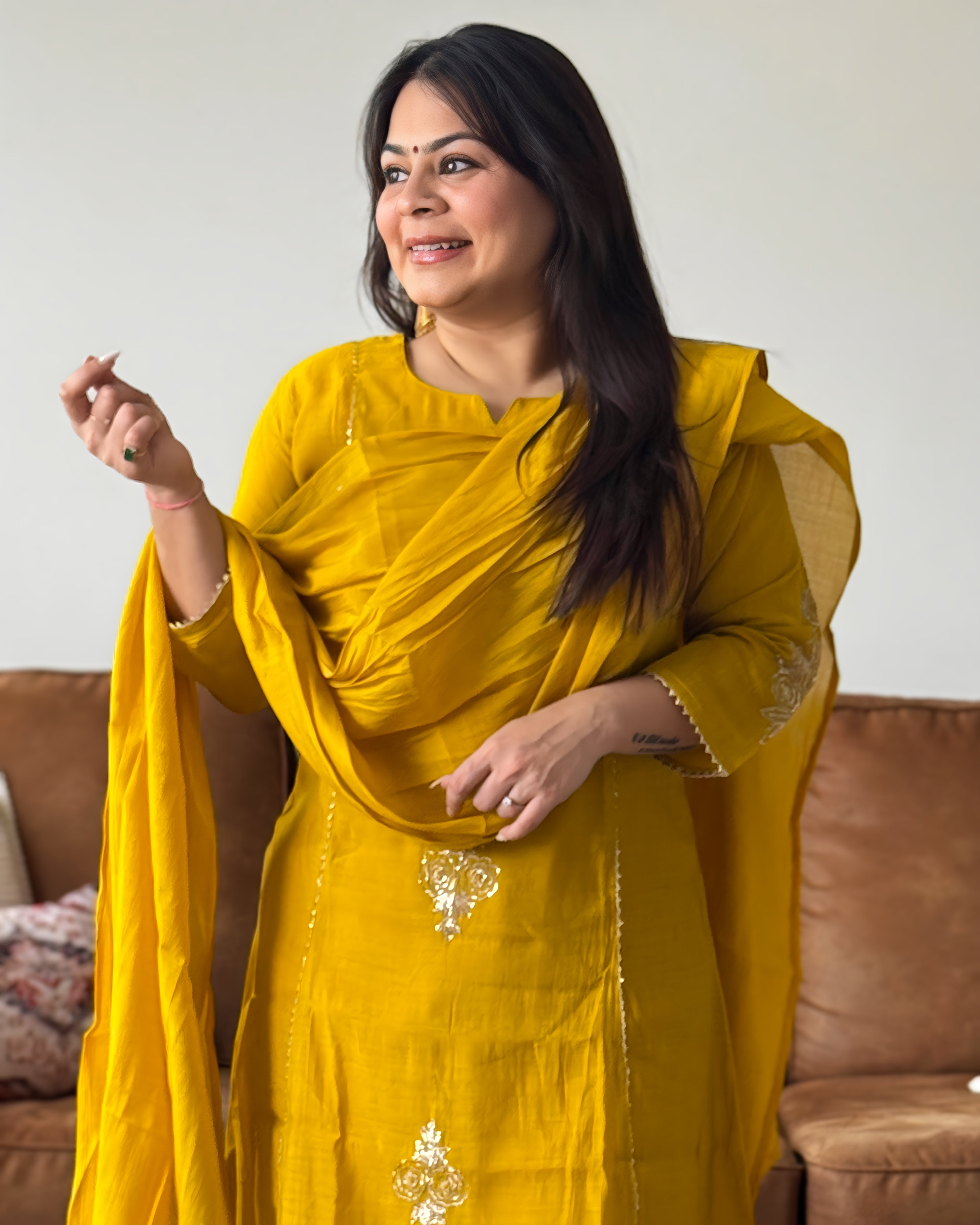 Woman wearing a yellow traditional outfit with a brown sofa in the background