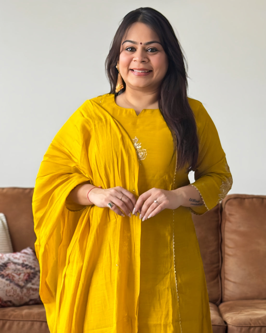 Woman wearing a yellow outfit standing in front of a brown couch.