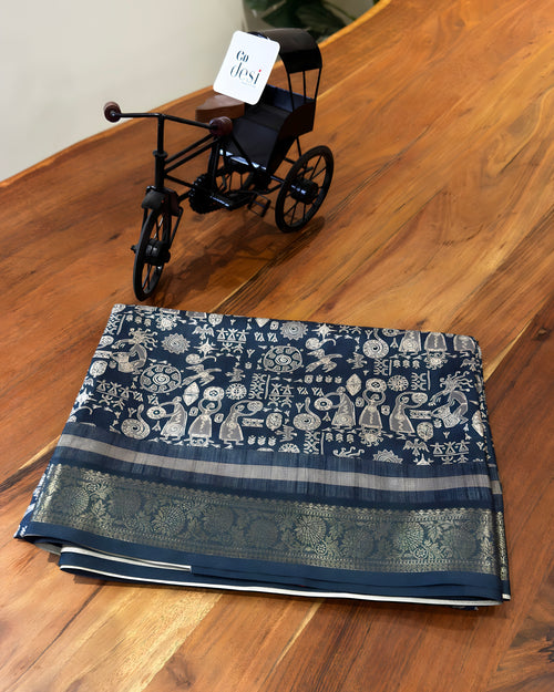 Folded fabric with intricate patterns on a wooden surface, accompanied by a small model vehicle.