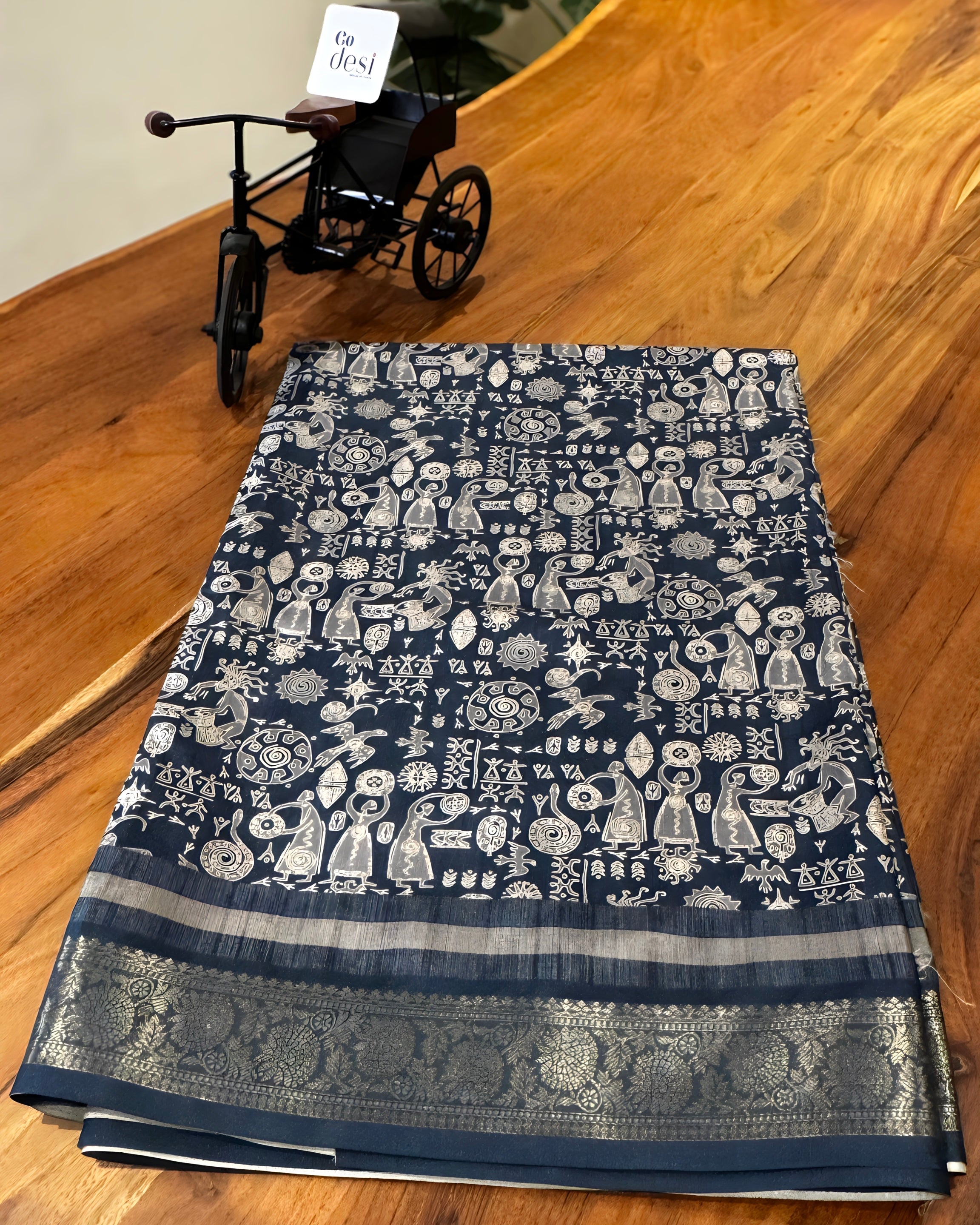 Blue patterned fabric on a wooden surface with a small black tricycle in the background.