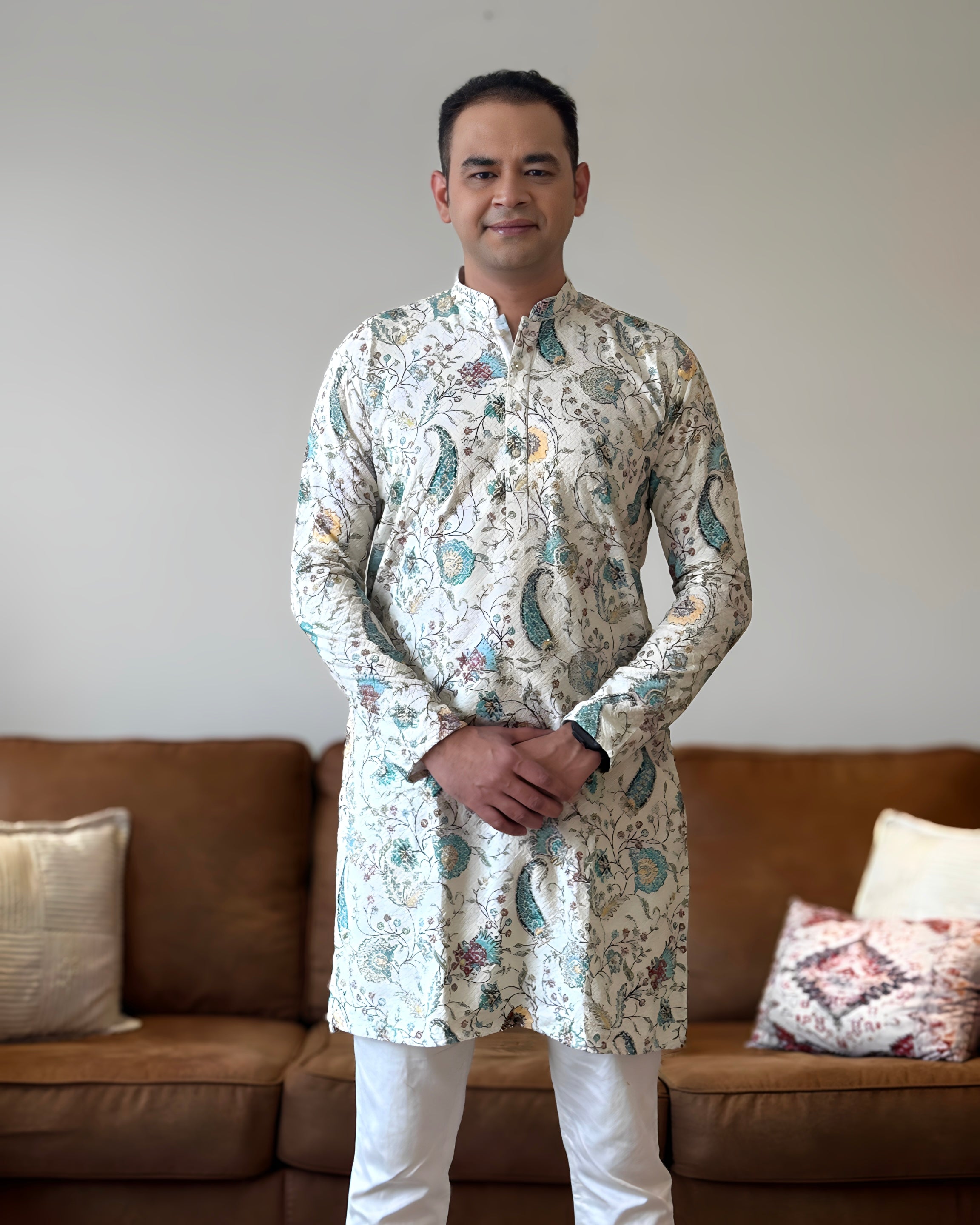 Man wearing a patterned kurta standing in a living room.