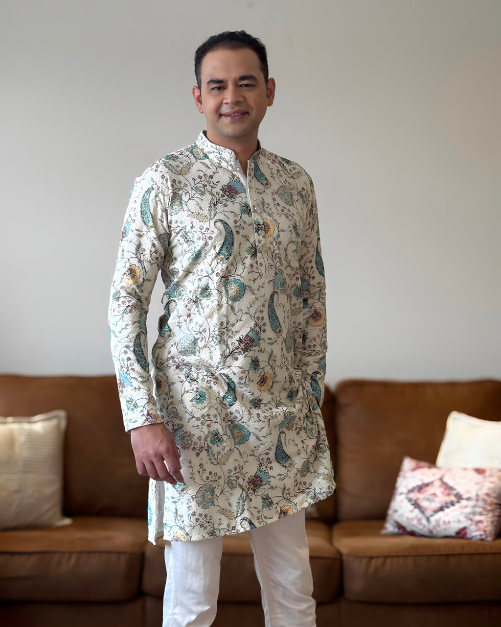 Man wearing a patterned kurta standing in a living room.