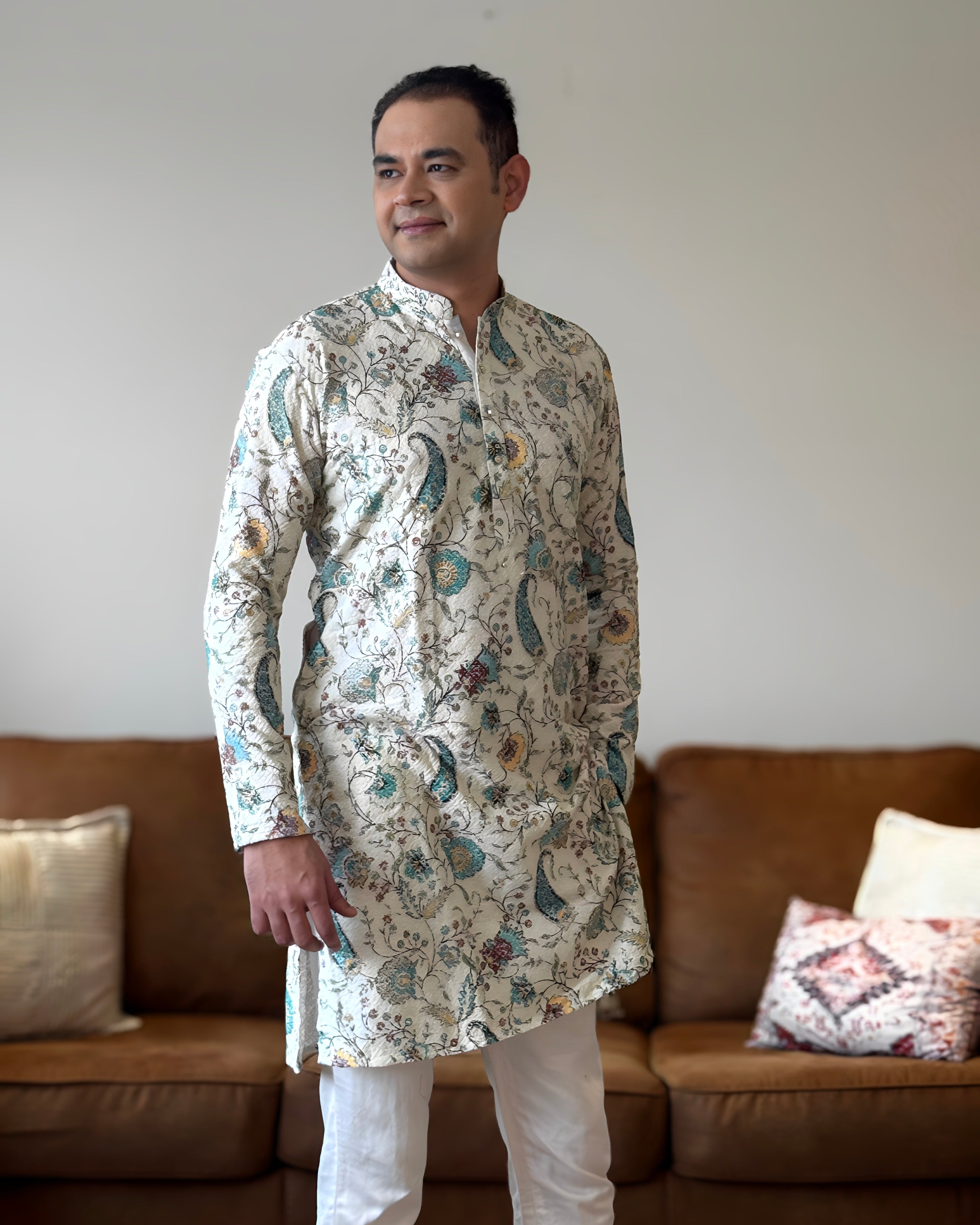 Man wearing a patterned kurta standing in a living room.
