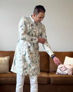 Man wearing a patterned kurta standing in a living room.