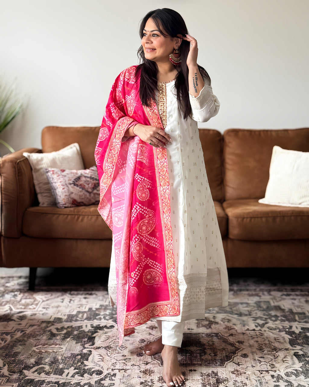 Woman wearing a white traditional outfit with a pink dupatta in a living room.
