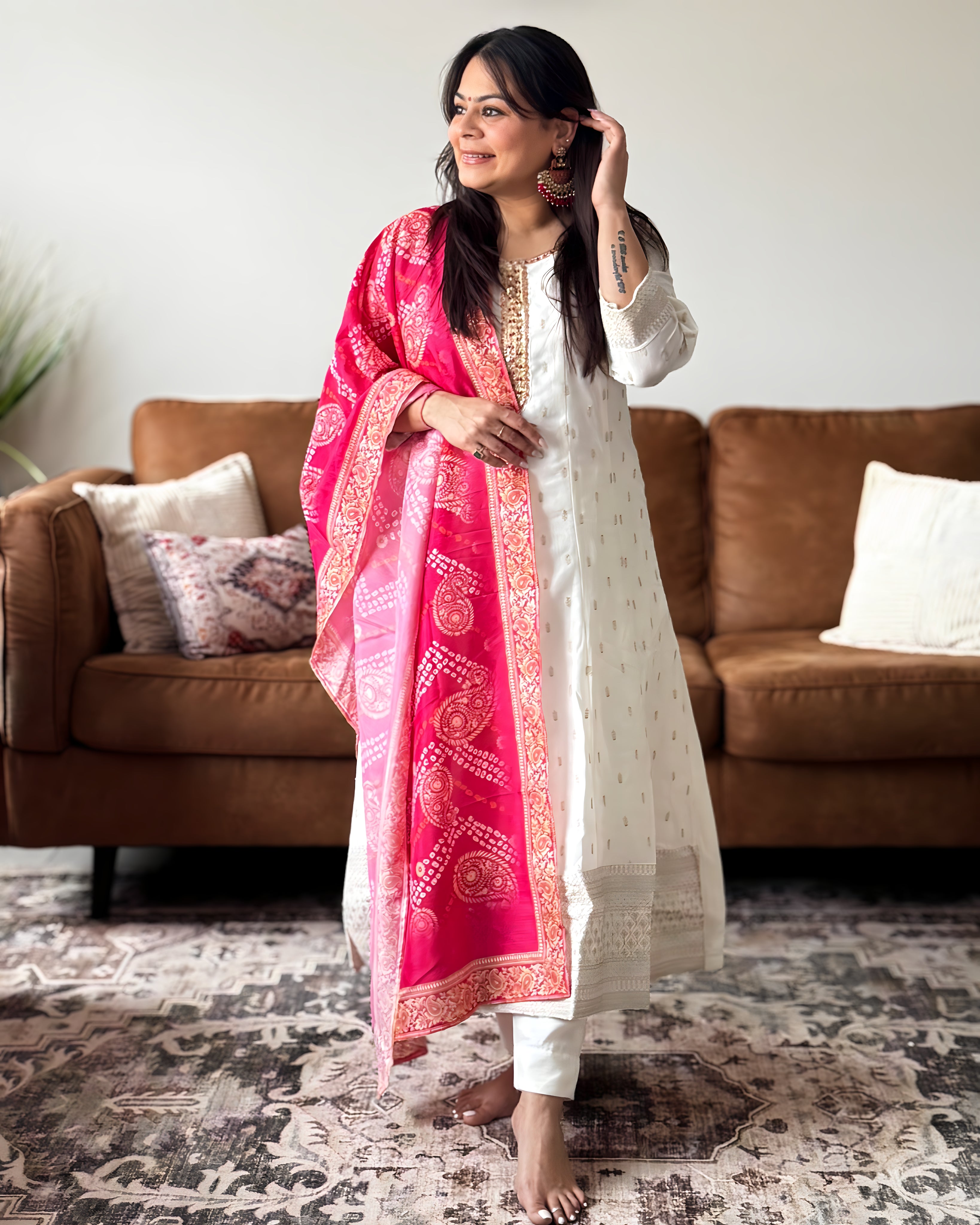 Woman wearing a white traditional outfit with a pink dupatta in a living room.