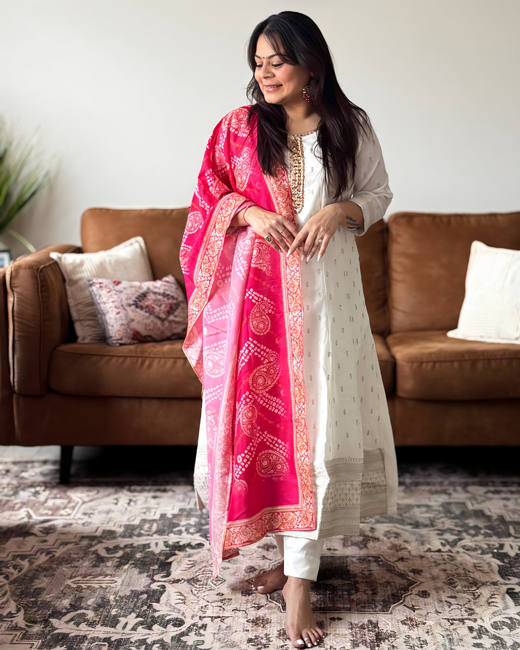 Woman in a white kurta with a pink dupatta standing in a living room.