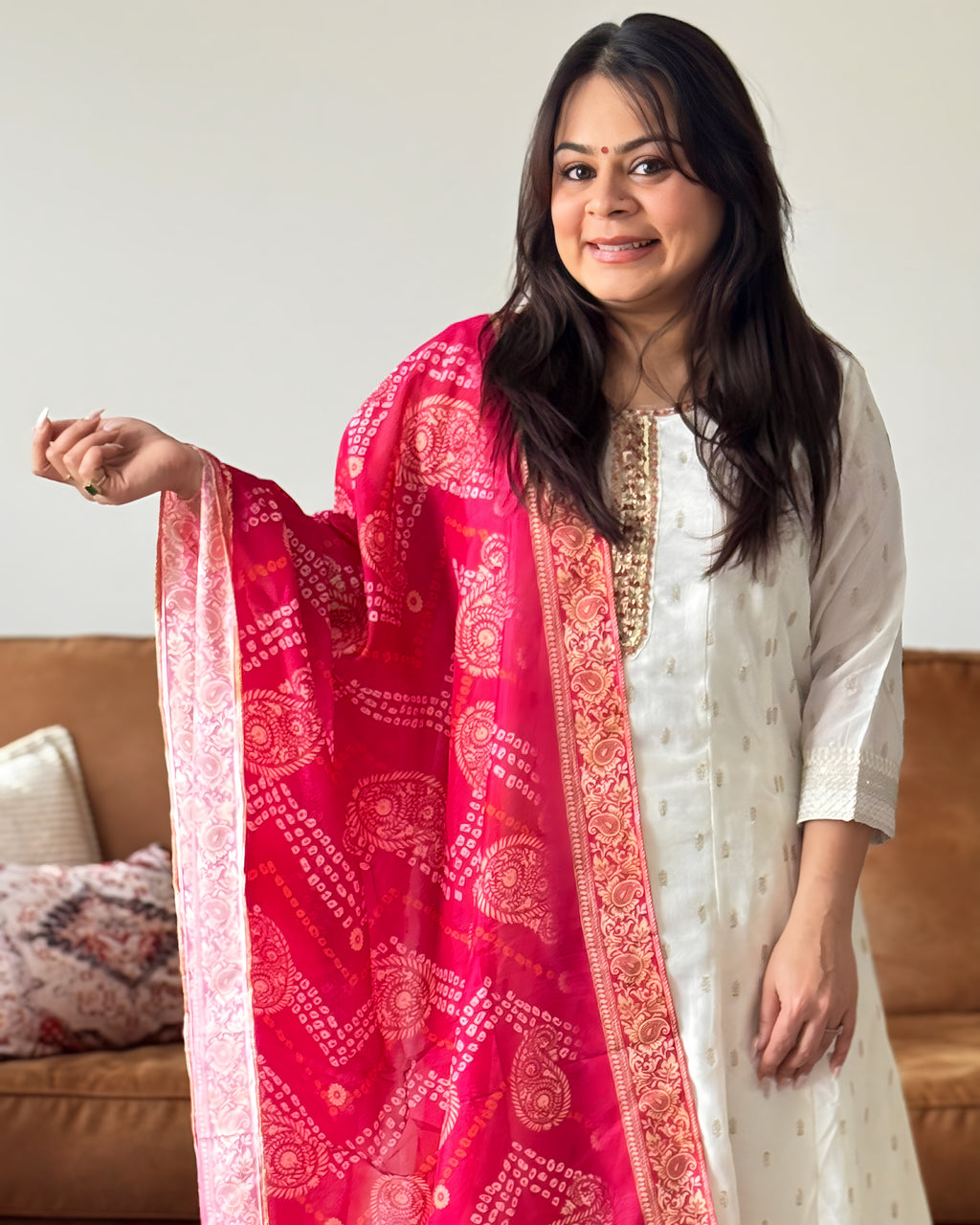 Woman holding a red and pink patterned scarf in front of a neutral background