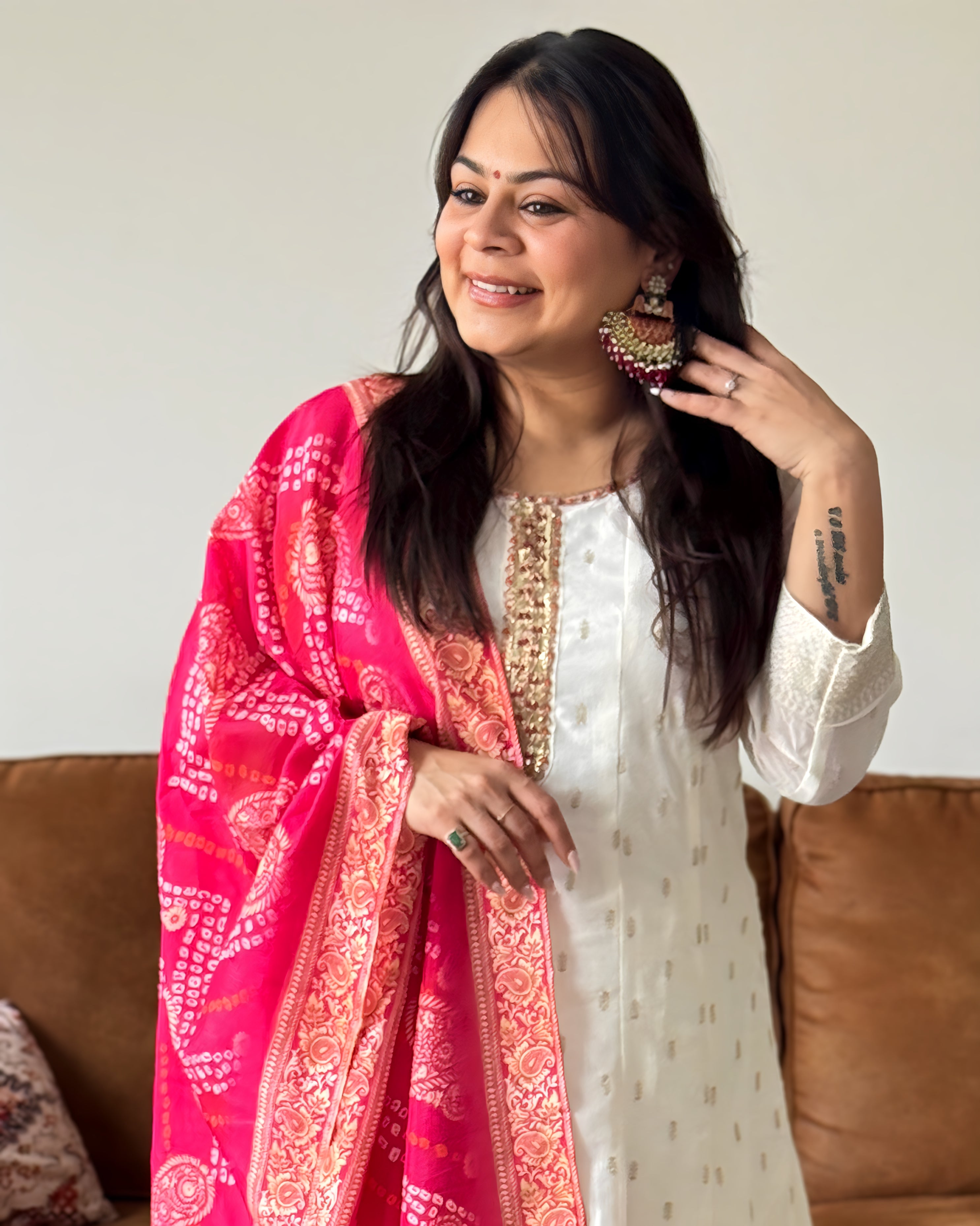 Woman wearing a white outfit with a pink and red patterned shawl, sitting on a brown couch.