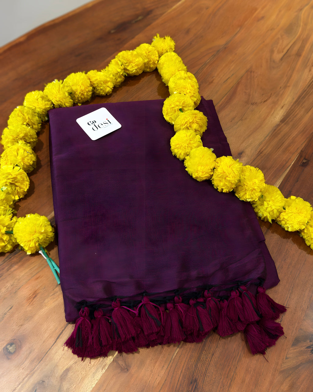 Purple fabric with tassels on a wooden surface, surrounded by yellow flowers.