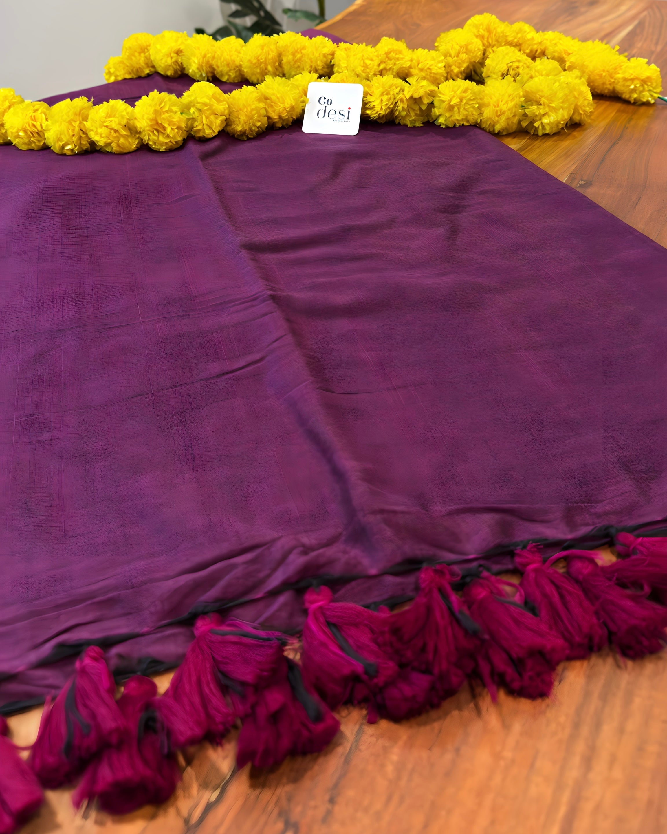 Purple fabric with red tassels on a wooden surface, accompanied by yellow flowers.