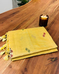 Yellow scarf with floral patterns on a wooden surface next to a lit candle.