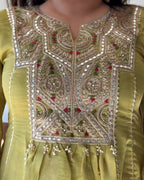 Close-up of a traditional embroidered kurta in olive green, featuring intricate gold and silver mirror work, beadwork, and small red floral accents on the yoke.