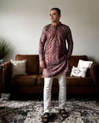 Man wearing a patterned kurta with white pants standing in a living room.