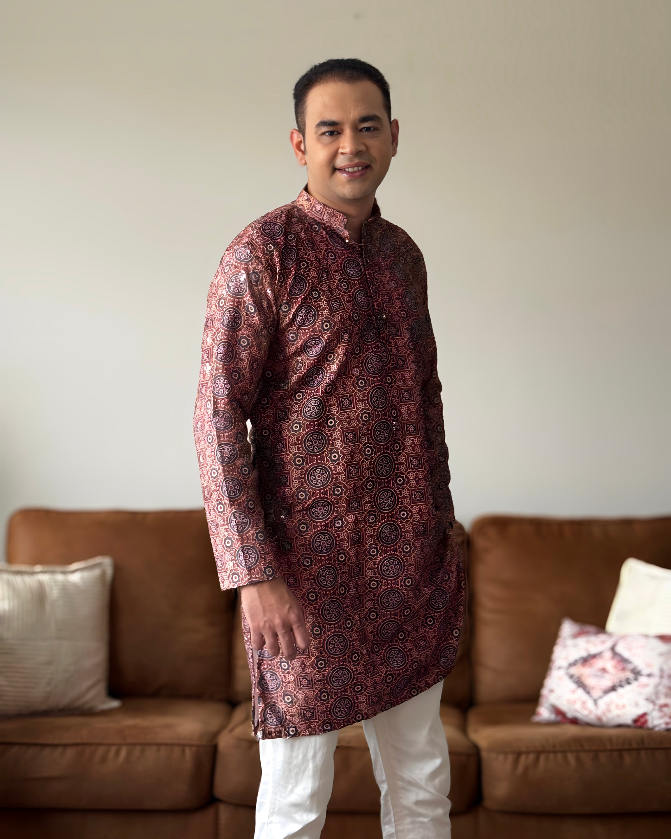 Man wearing a patterned kurta standing in a living room.