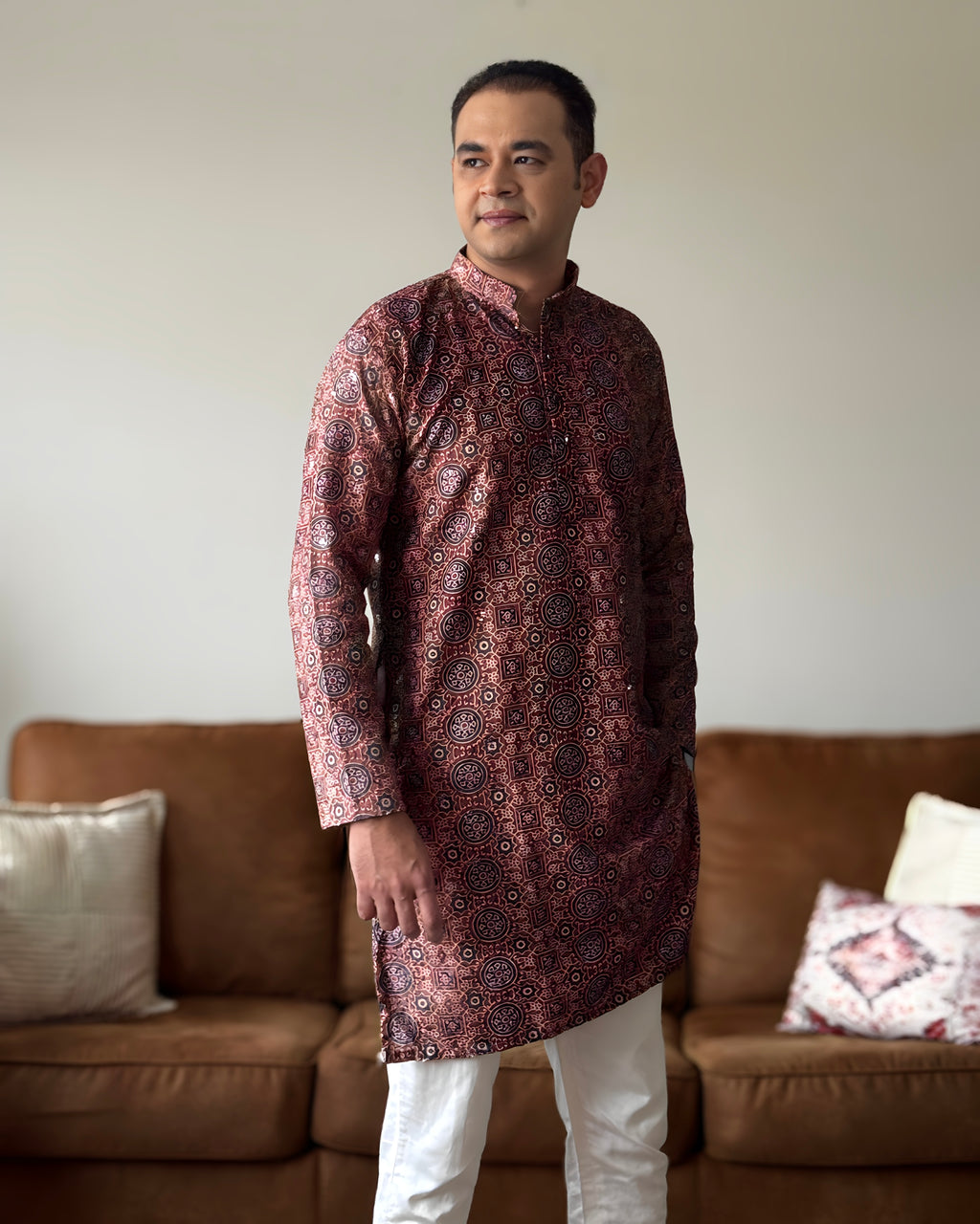 Man wearing a patterned kurta standing in a living room.