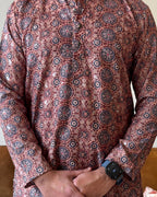 Person wearing a patterned shirt with a watch on a wooden floor.