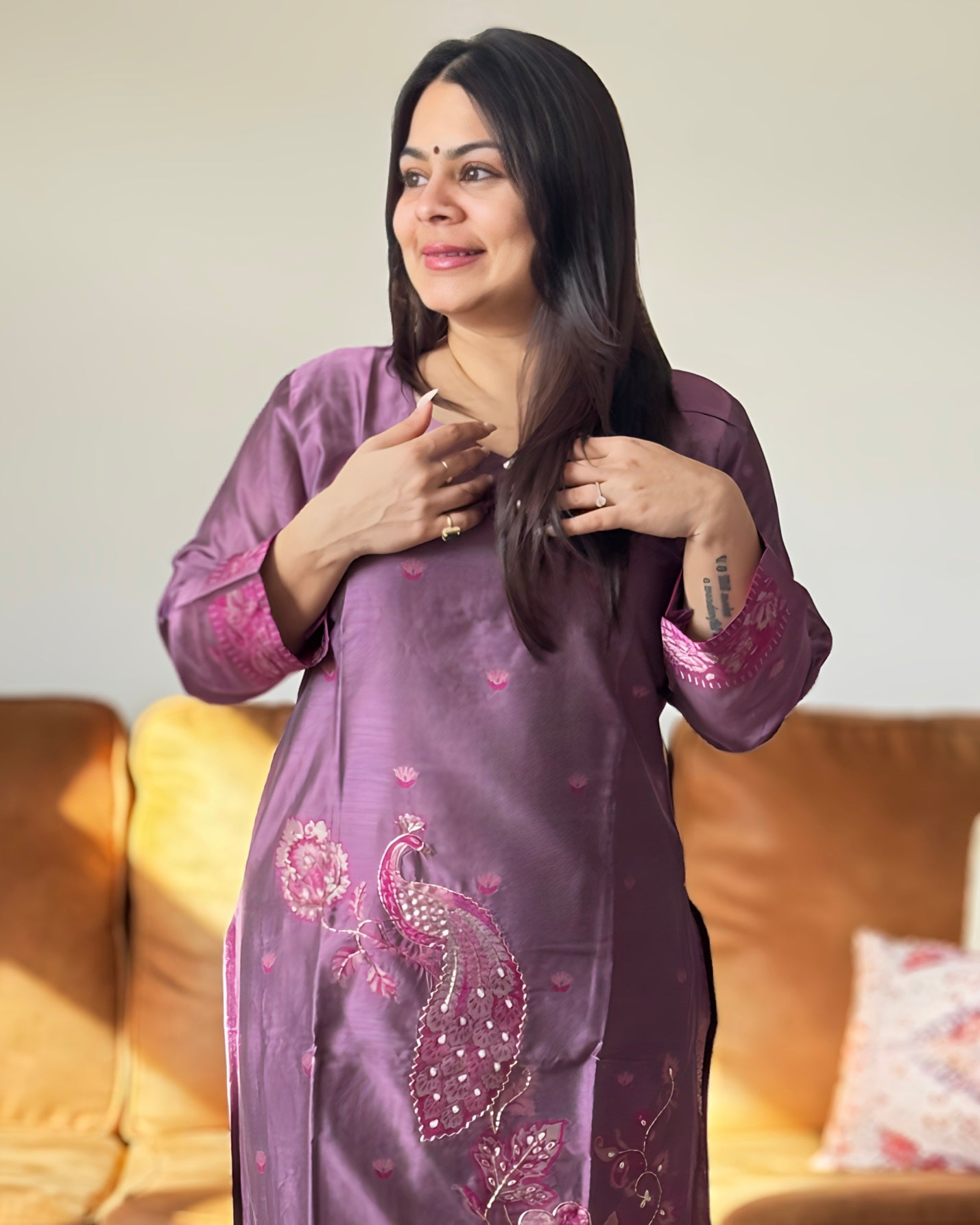 Woman wearing a purple embroidered traditional outfit sitting on a couch.