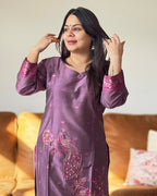 Woman wearing a purple embroidered traditional outfit sitting on a couch.