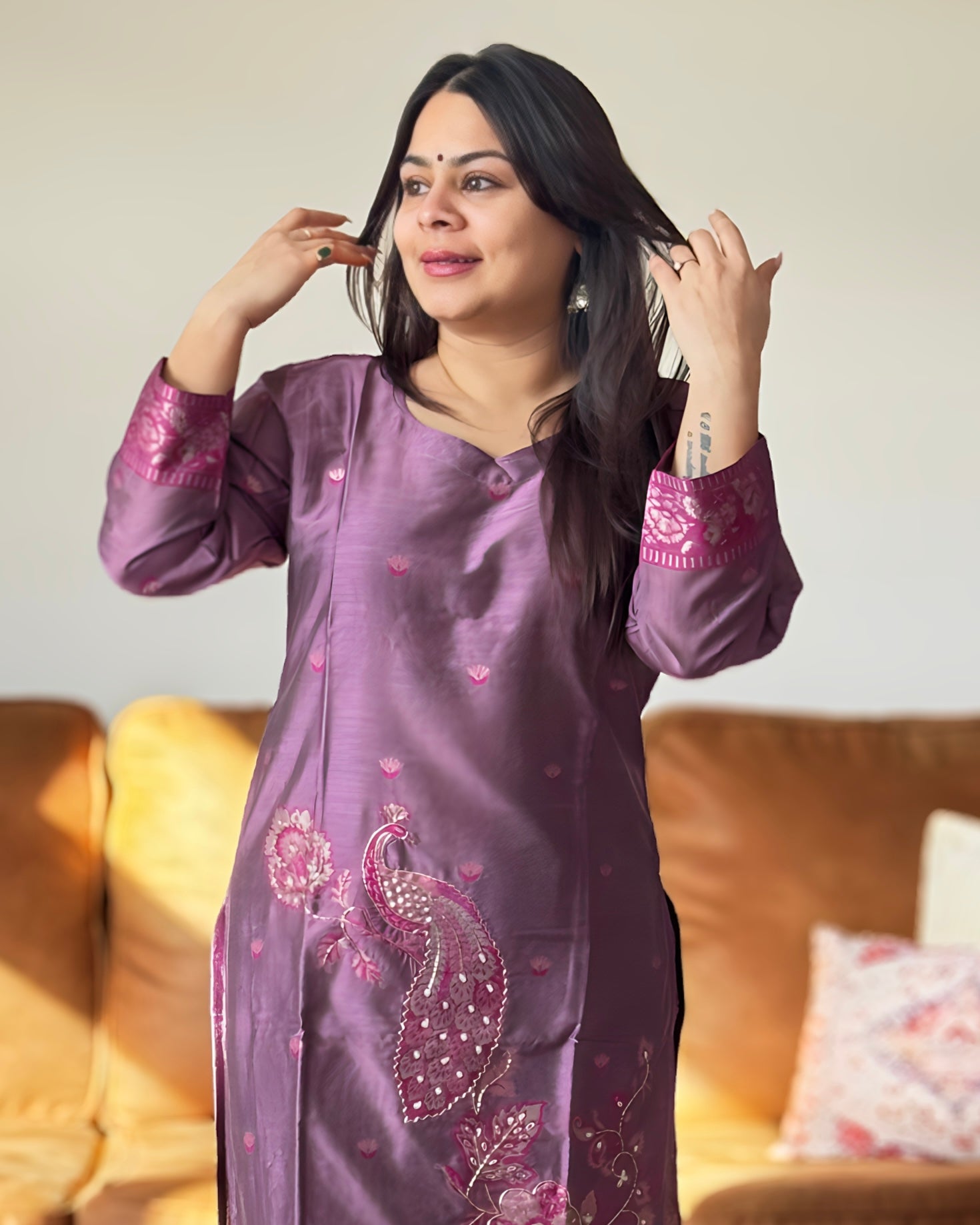 Woman wearing a purple embroidered traditional outfit sitting on a couch.