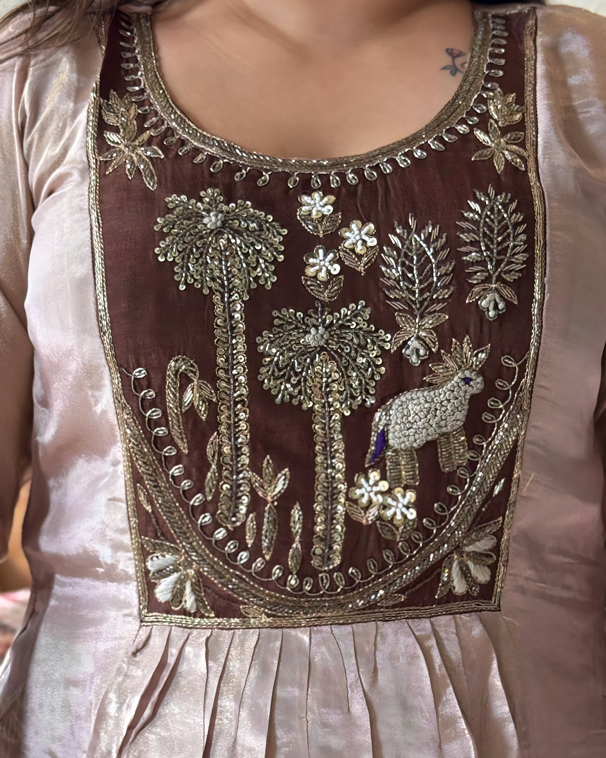 Close-up of a brown embroidered dress bodice with metallic gold and silver mirror work, floral motifs, and a small peacock embellishment, worn by a model.