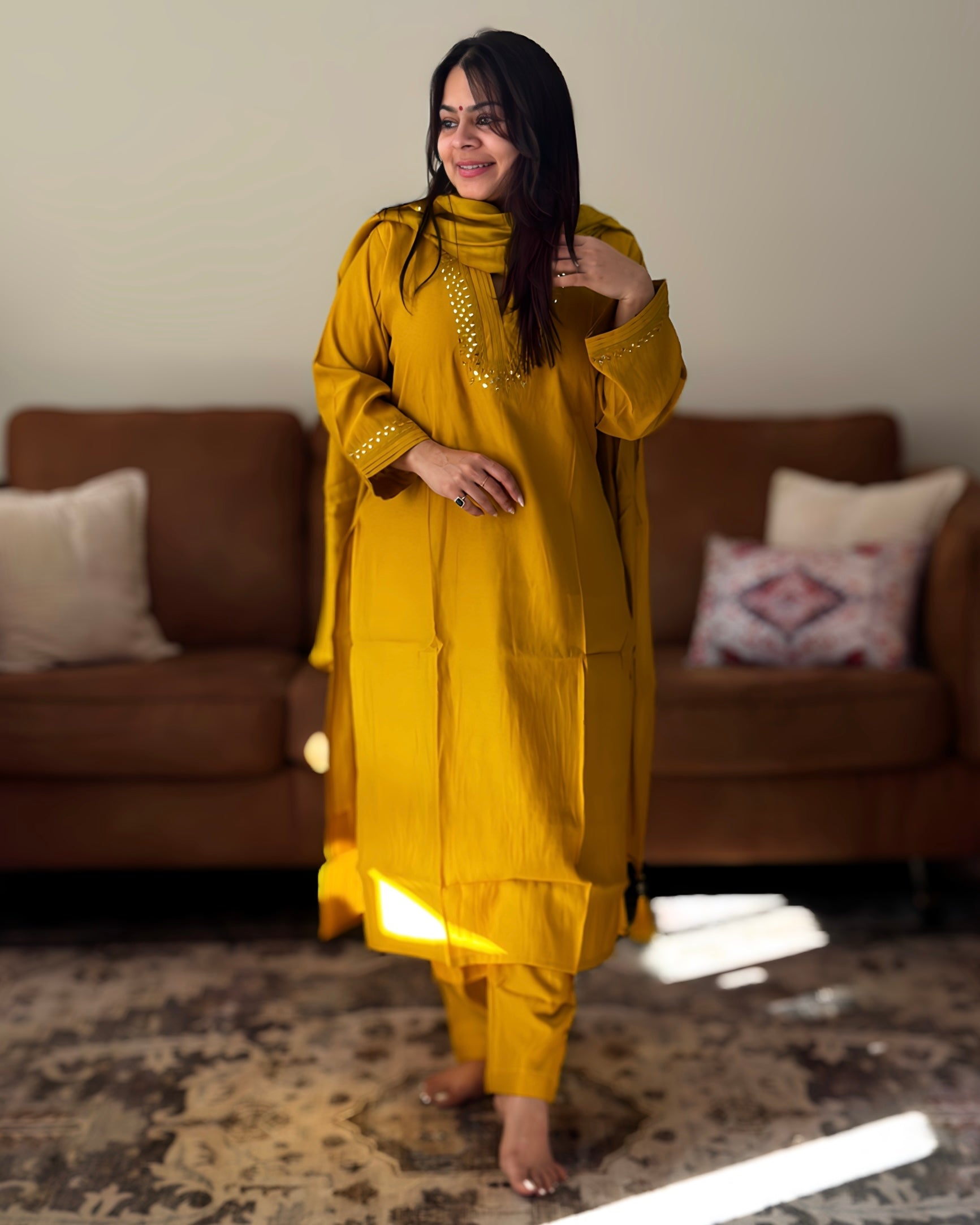 Woman in a mustard yellow traditional outfit standing in a living room.