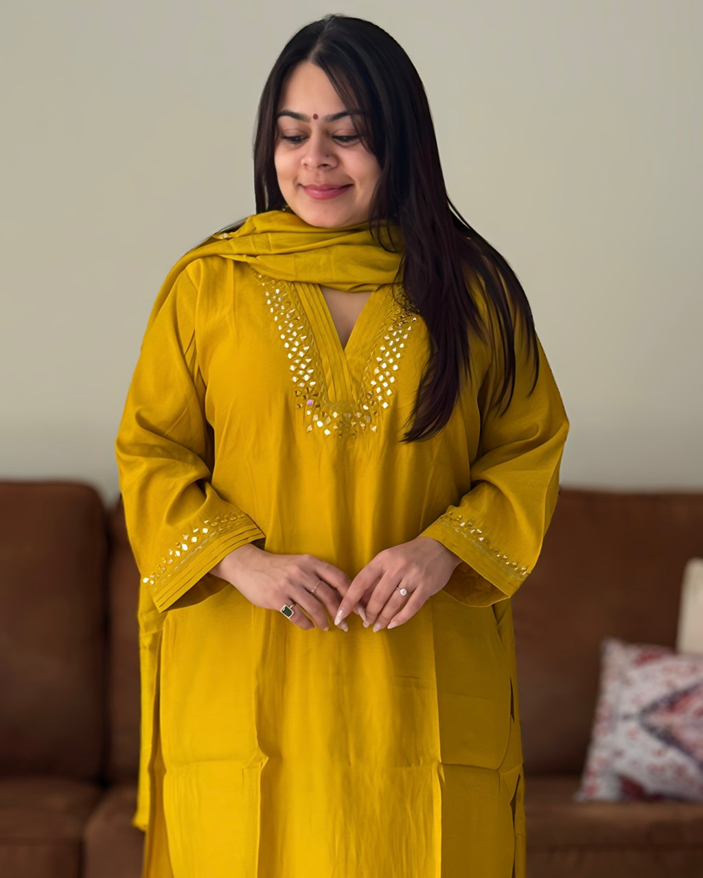 Woman wearing a mustard yellow traditional outfit with a matching dupatta in a living room setting.