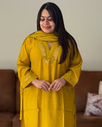 Woman wearing a mustard yellow traditional outfit with a matching dupatta in a living room setting.