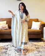 Woman in a beige and black traditional outfit standing in a living room.