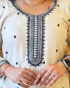 Close-up of a person wearing a white top with black embroidery, hands in front.