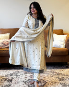 Woman holding a white saree with black patterns in a living room.