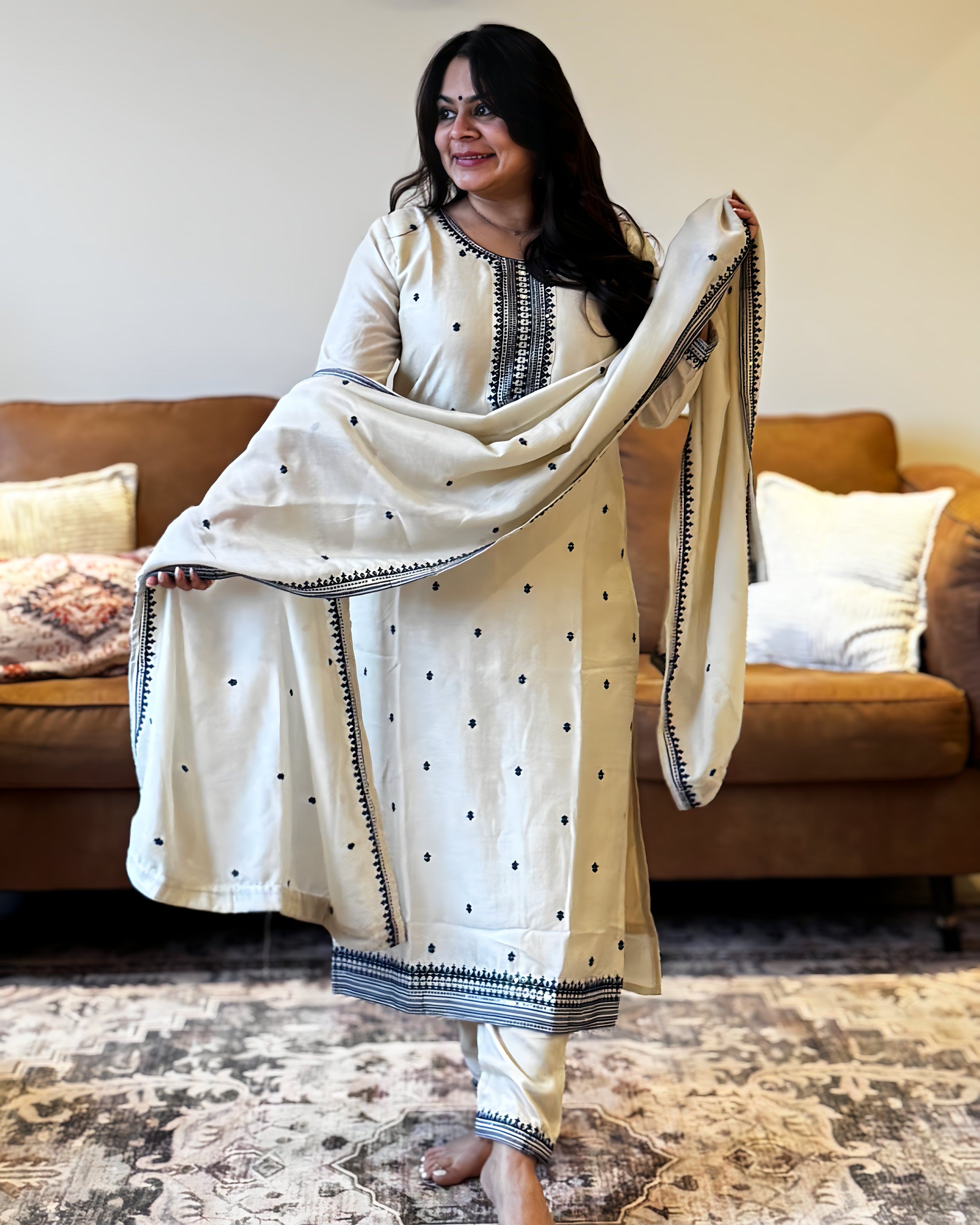 Woman holding a white saree with black patterns in a living room.