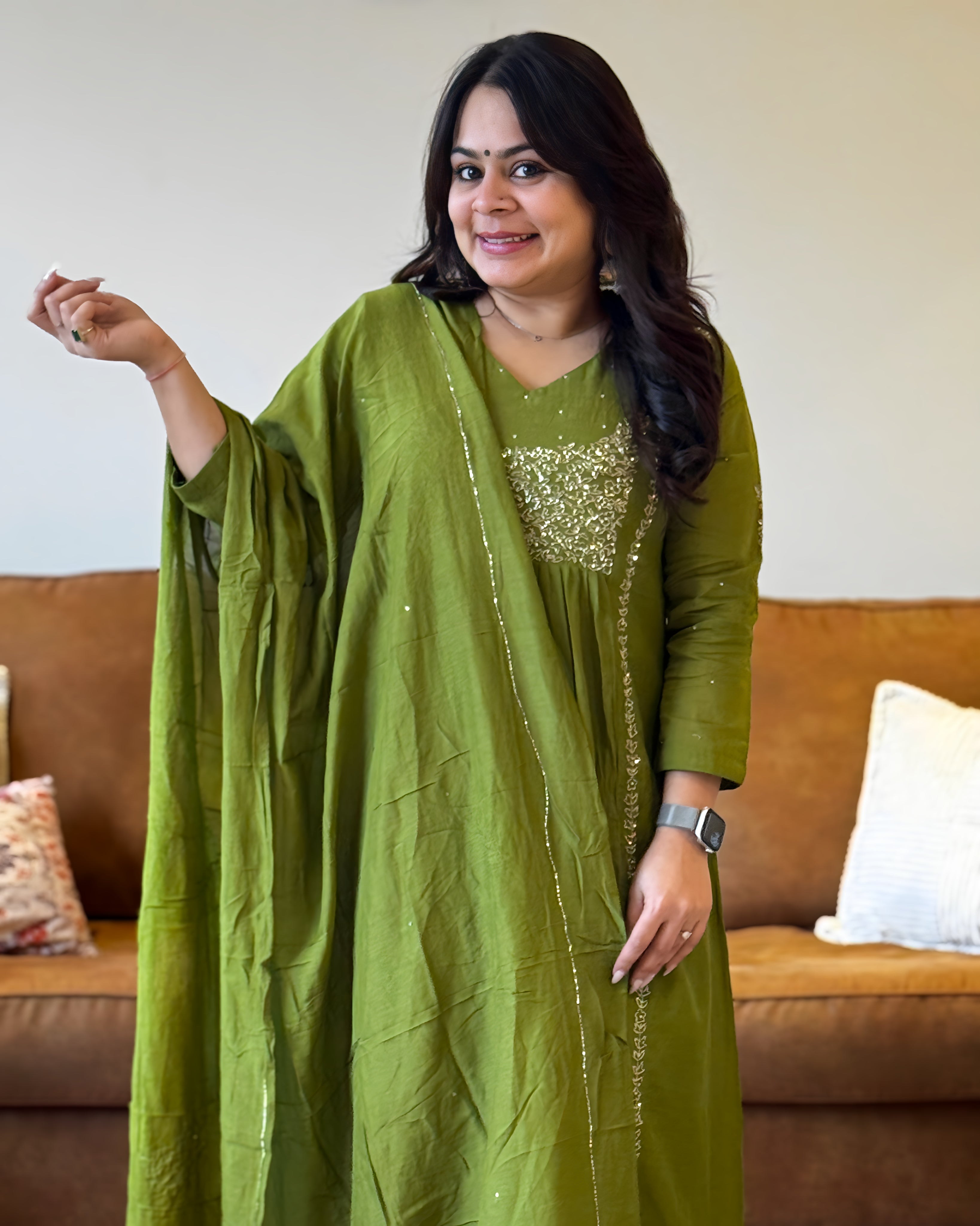 Woman wearing a green traditional outfit with a brown sofa in the background