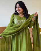 Woman wearing a green traditional outfit with a matching dupatta, sitting on a couch.