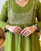 Green dress with silver embroidery worn by a person, with a neutral background.