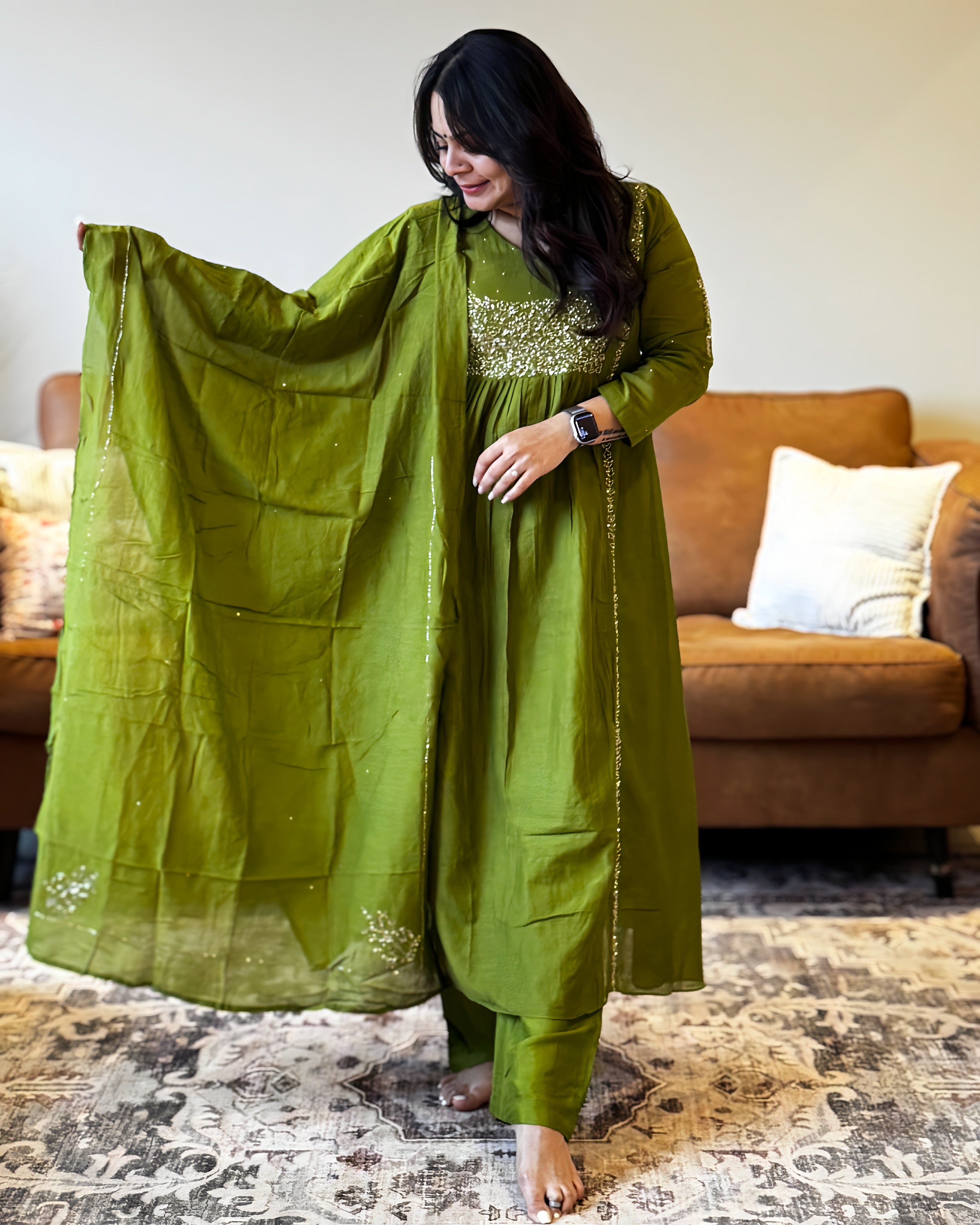 Woman wearing a green traditional outfit with a matching dupatta in a living room setting.