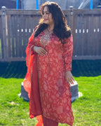 Woman in a red floral dress standing outdoors on grass with a wooden fence in the background