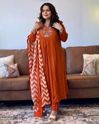 Woman wearing an orange traditional outfit with a chevron patterned dupatta in a living room.
