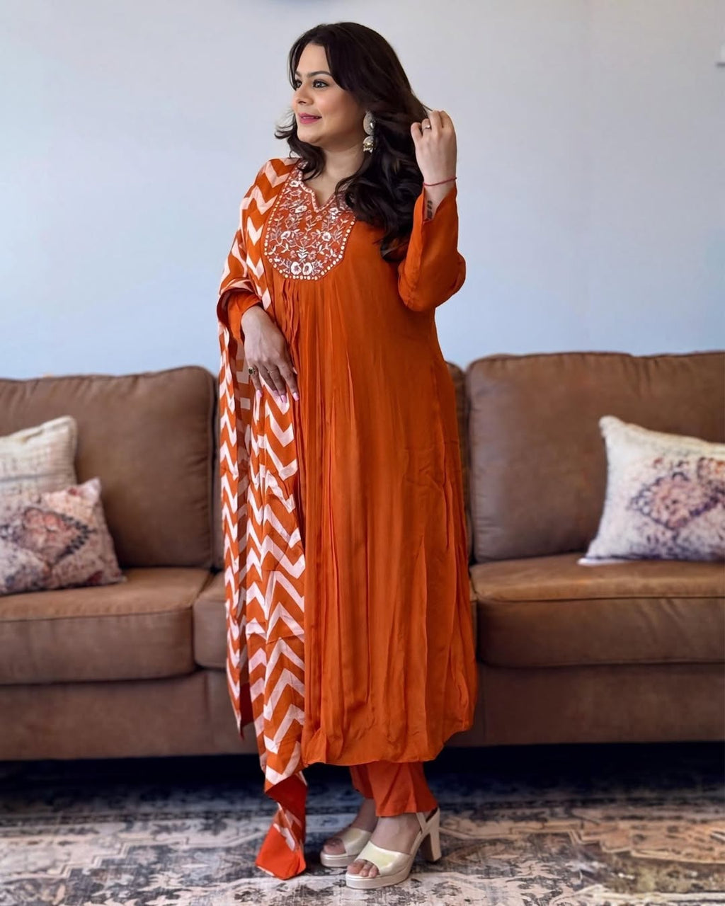 Woman in an orange traditional outfit with a chevron pattern standing in a living room.