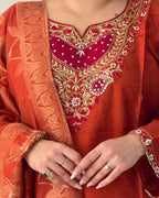 Close-up of a person wearing an orange embroidered traditional outfit with gold and red details.