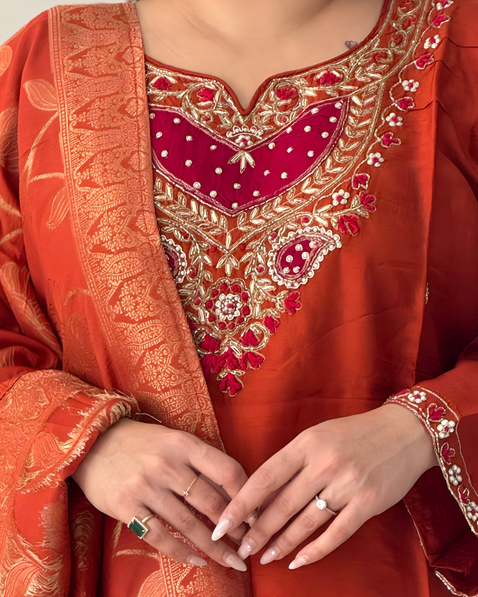 Close-up of a person wearing an orange embroidered traditional outfit with gold and red details.