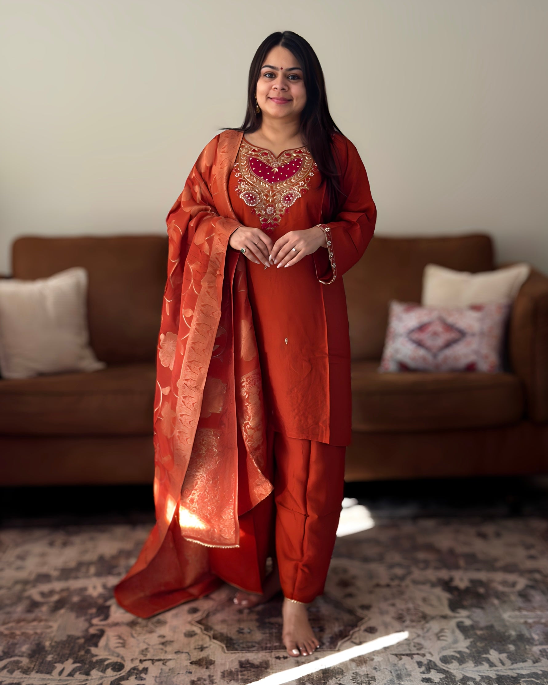 Woman in an orange traditional outfit standing in a room with a couch and pillows.
