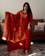 Woman in traditional red outfit with gold patterns standing in a room.