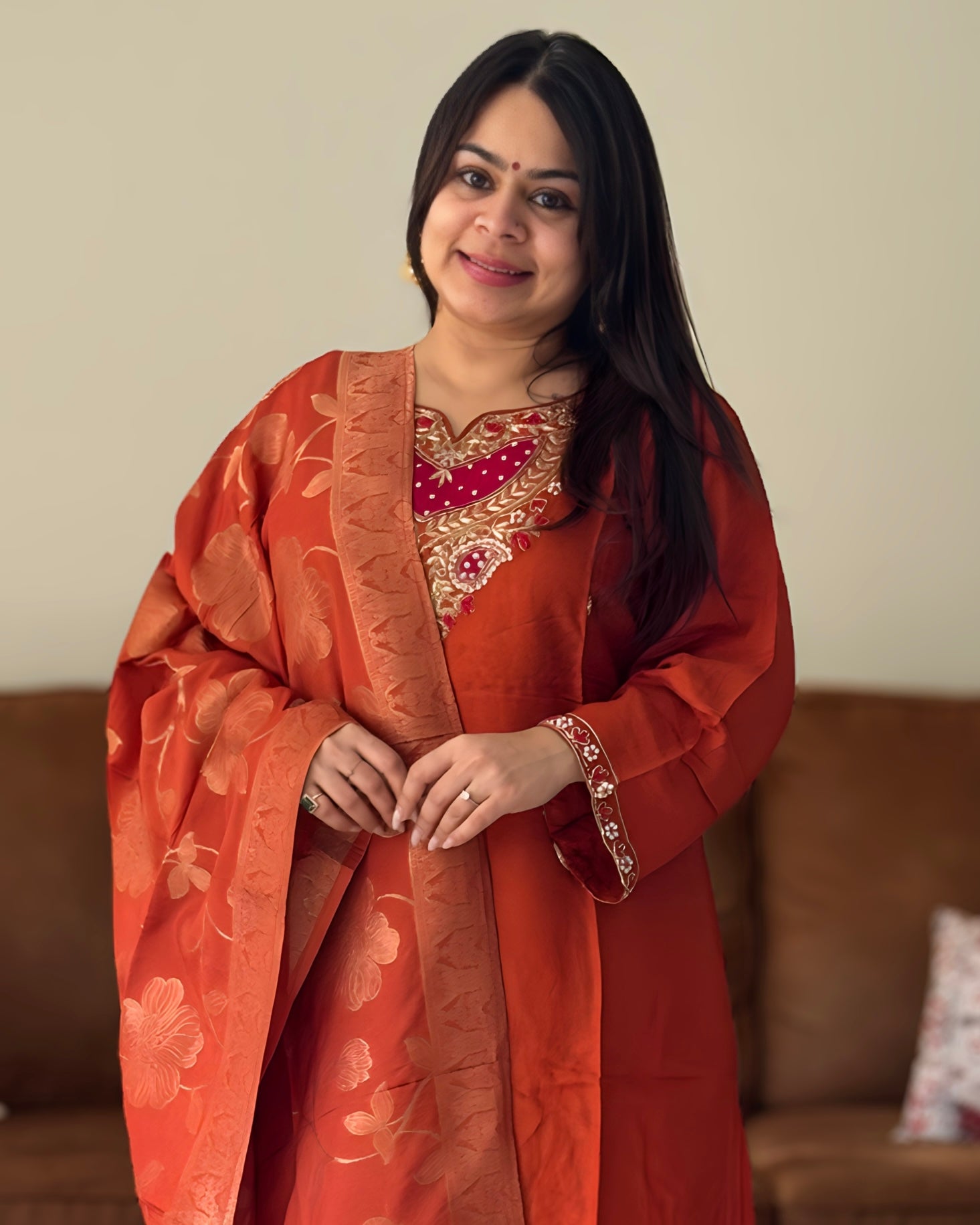 Woman wearing an orange traditional outfit with floral patterns indoors.
