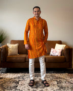 Man wearing an orange kurta with white pants standing in a living room.