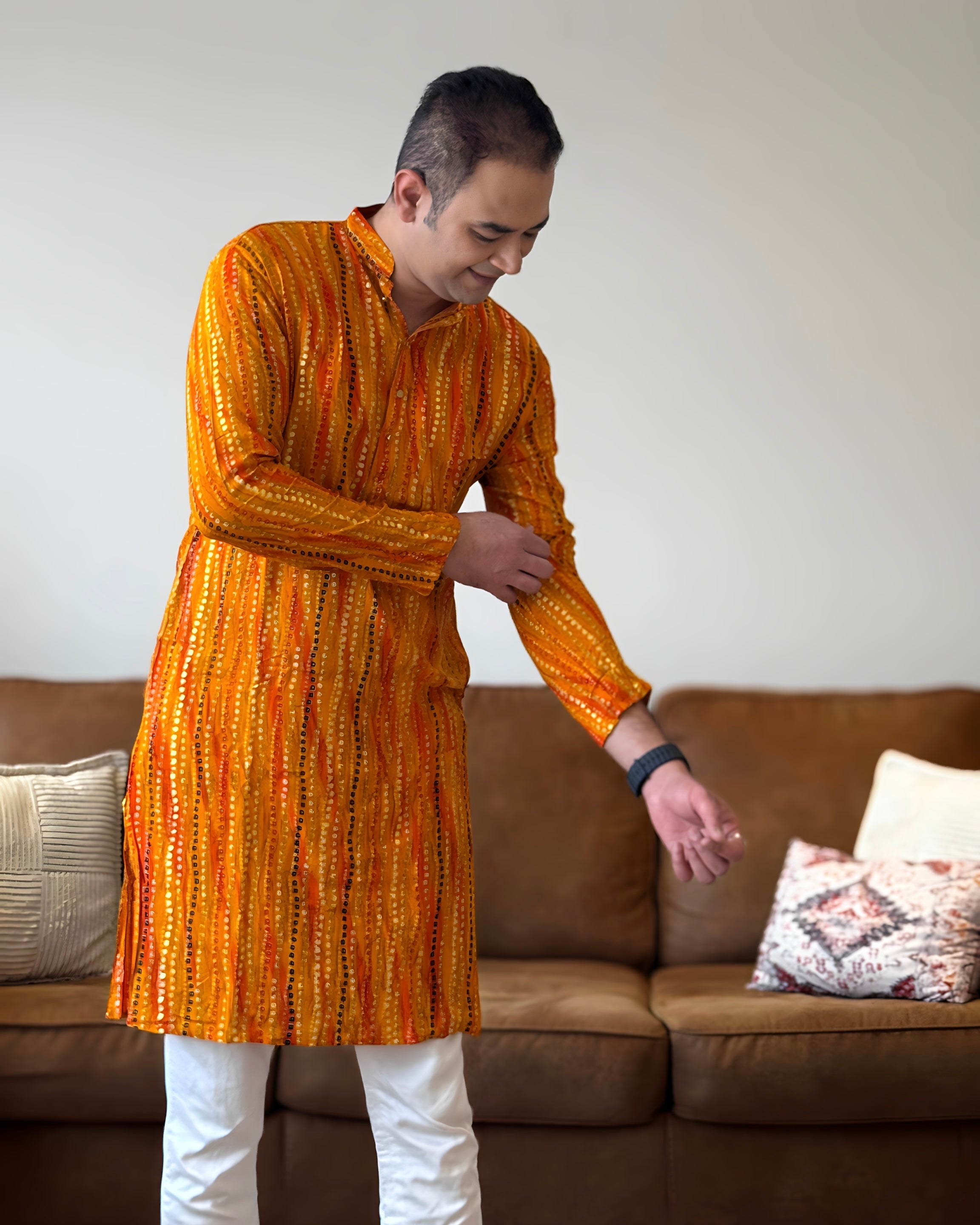 Man wearing an orange patterned kurta standing in a living room.