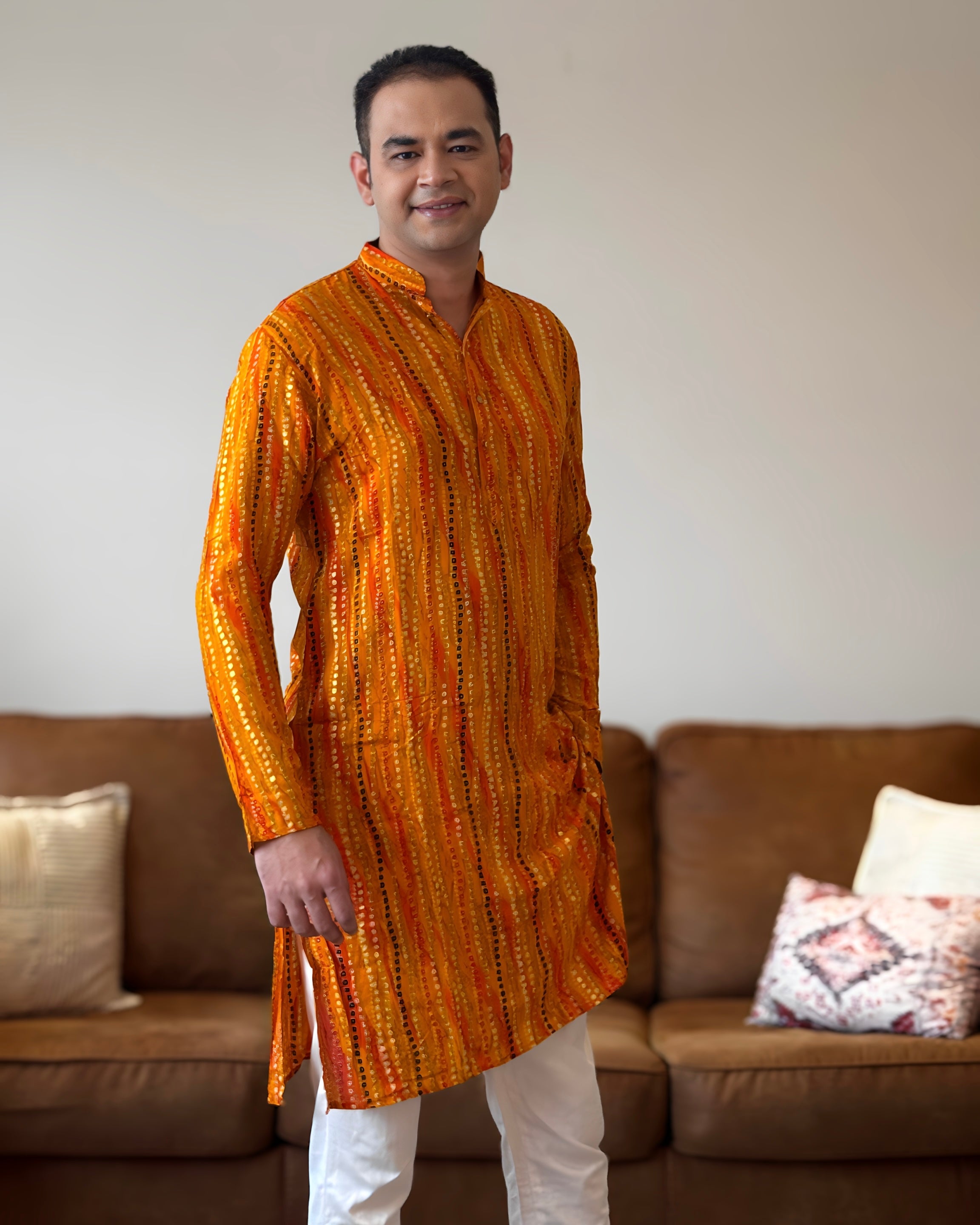 Man wearing an orange kurta with white pants standing in a living room.
