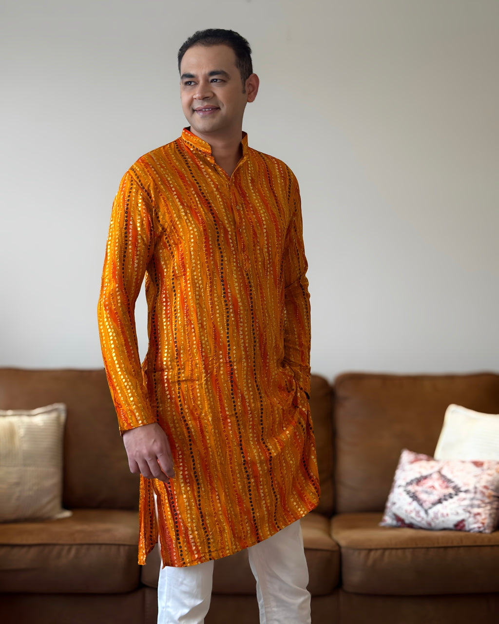 Man wearing an orange kurta standing in a living room.