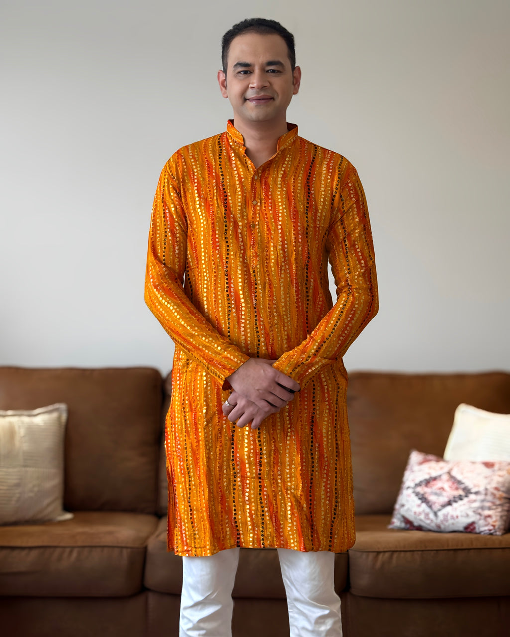 Man wearing an orange and yellow patterned kurta standing in a living room.